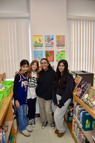 group of students in a library proudly display colorful books, smiling, during a book fair.