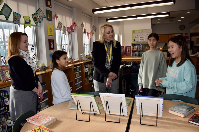 group of students in a library proudly display colorful books, smiling, during a book fair.