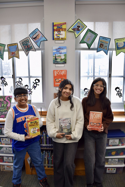 group of students in a library proudly display colorful books, smiling, during a book fair.