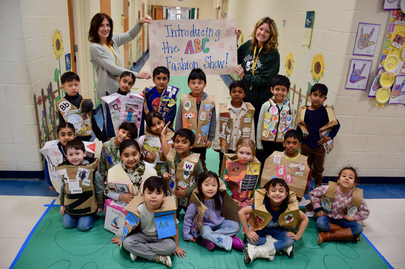 A group of young children and a teacher pose in a decorated school hallway.