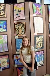 Student standing proudly in front of art exhibit.