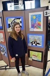 Student standing proudly in front of art exhibit.