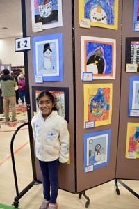 Student standing proudly in front of art exhibit.