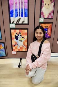 Student standing proudly in front of art exhibit.