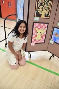 Student standing proudly in front of art exhibit.