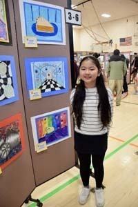 Student standing proudly in front of art exhibit.