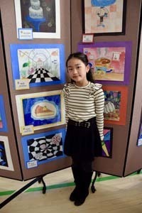 Student standing proudly in front of art exhibit.