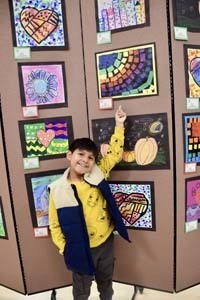 Student standing proudly in front of art exhibit.
