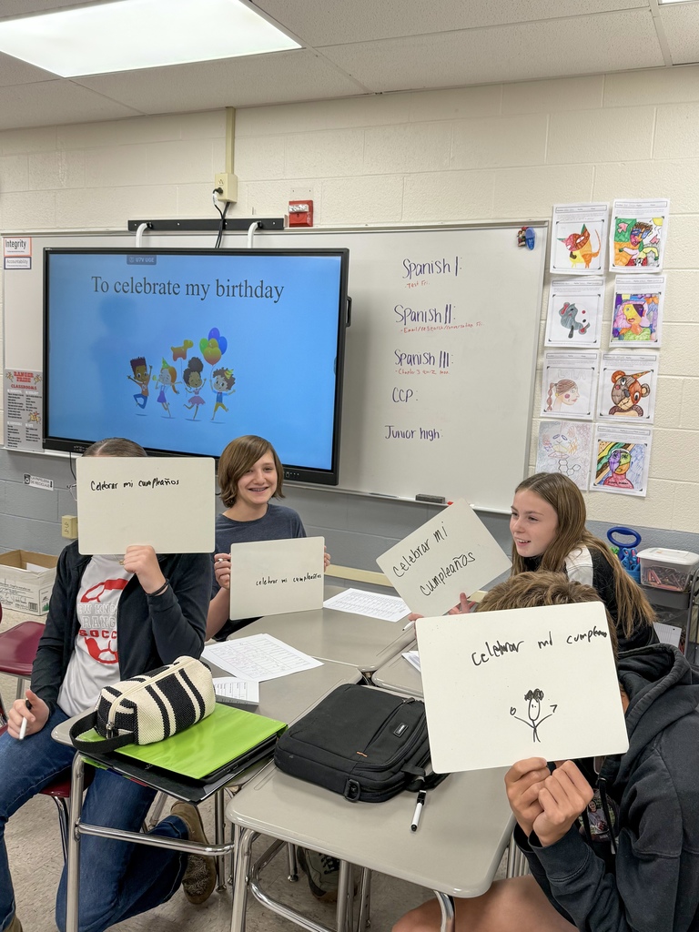 Students are holding up small whiteboards that say "celebrar mi cumplea~nos". 