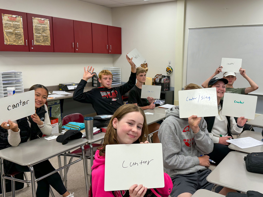 Students are holding up small whiteboards that say "cantar". 
