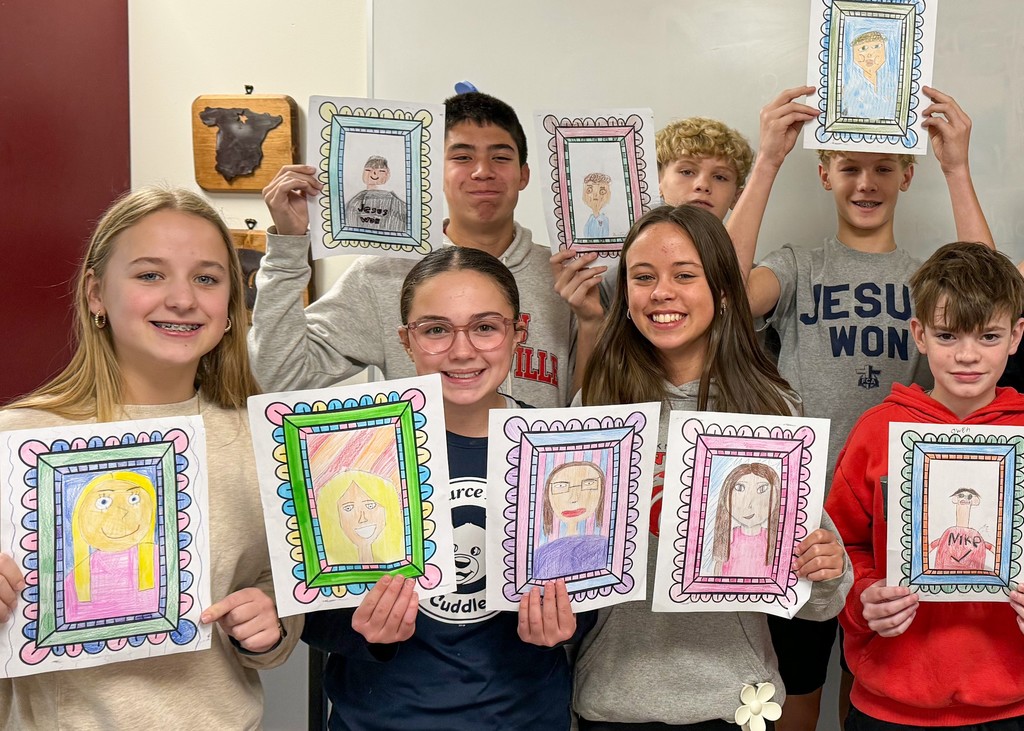Various students holding up their self portraits. 