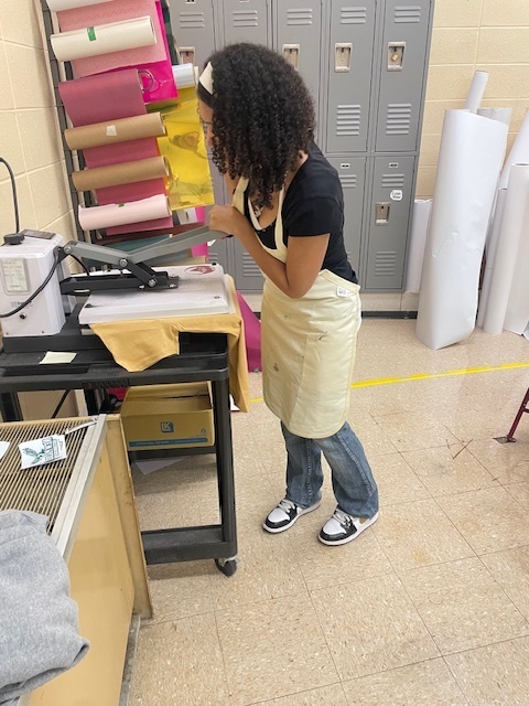 A student using the heat press to finish a shirt.