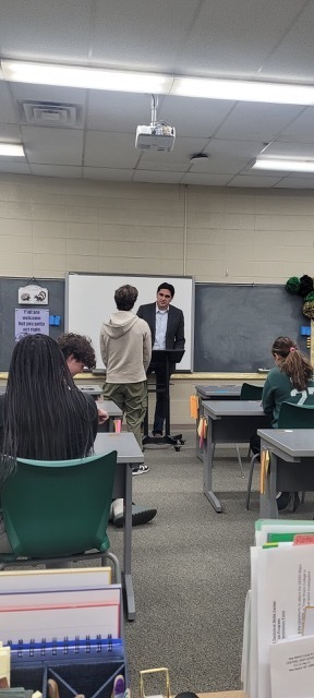 A student and mand standing at the front of a classroom.