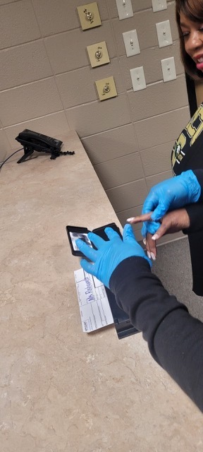 A pair of hands in blue gloves fingerprinting another hand.