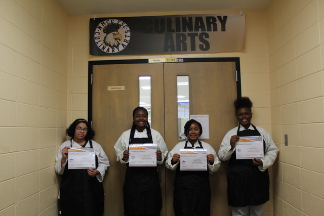 Four students with aprons on, holding their ServSafe food Handler certificate.