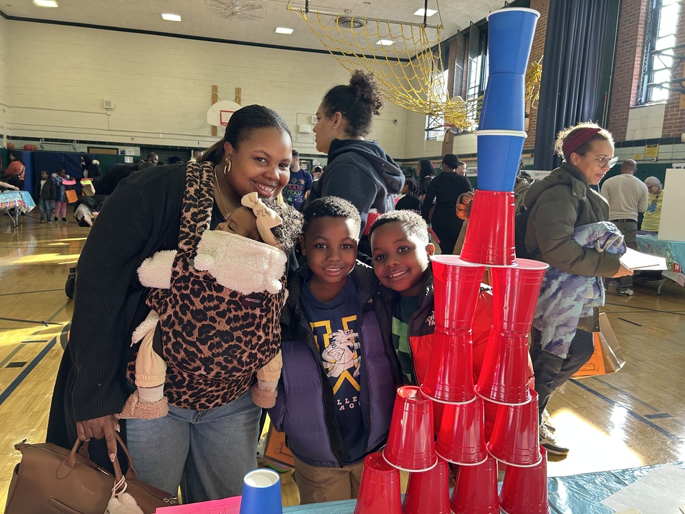 A family smiling at the camera with a stack of cups in front of them