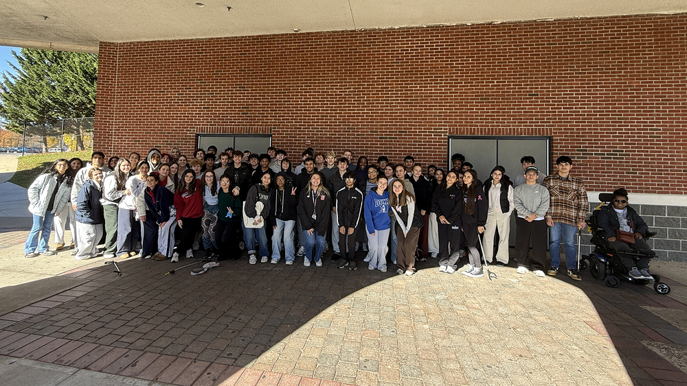 A large group of students pose for a photo in front of a brick building