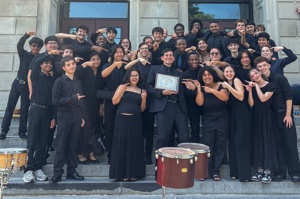 a group photo of the wind symphony pointing at their conductor and laughing