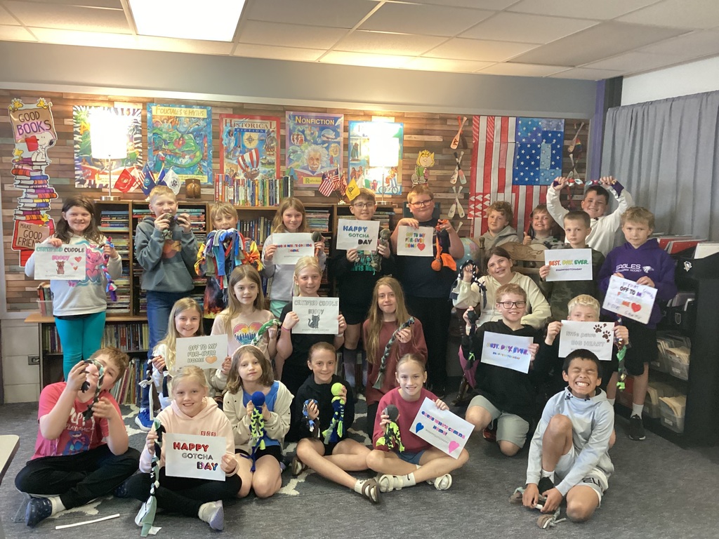 A class of students holding the dog toys they made and signs that say "Happy Gotcha Day".