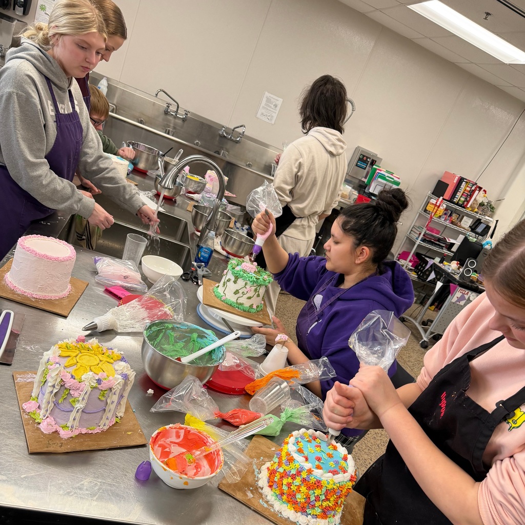 Students gathered around a table, decorating their cakes, nearly finished.