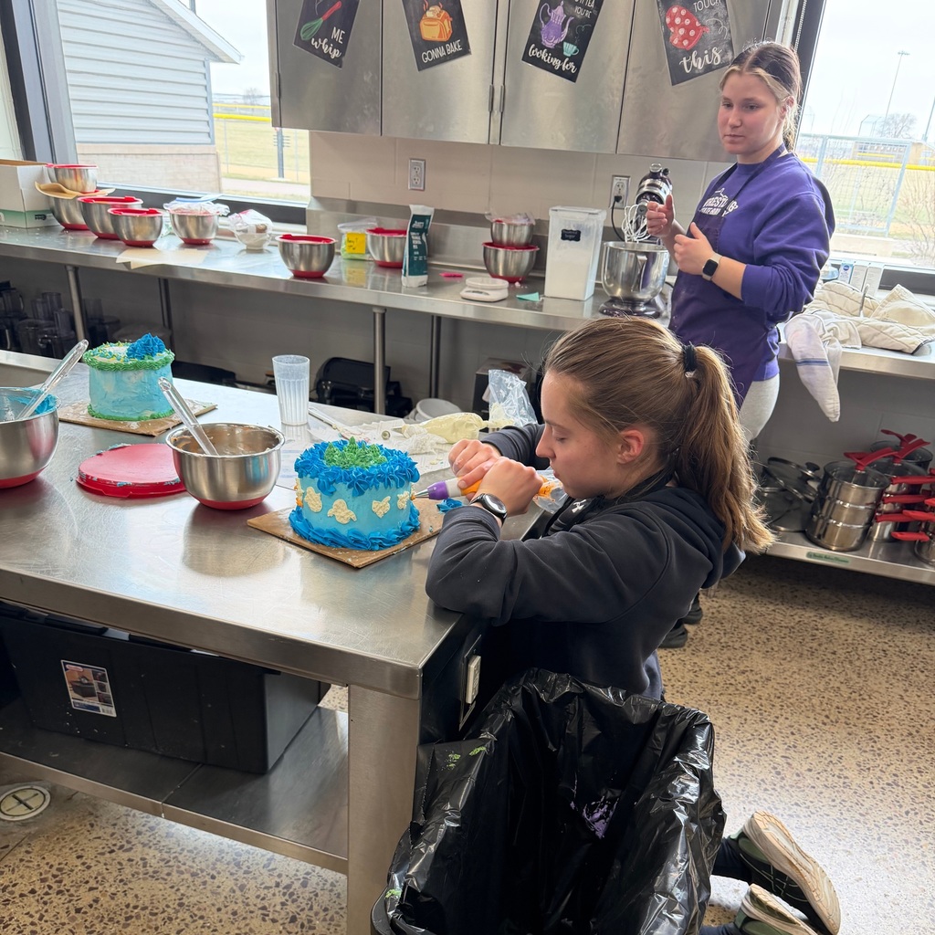 A student at a table, decorating her cake with birds made of frosting.