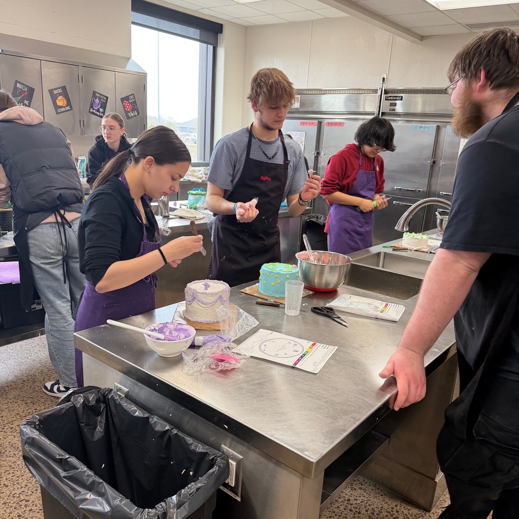 Students gathered around a table, decorating their cakes.