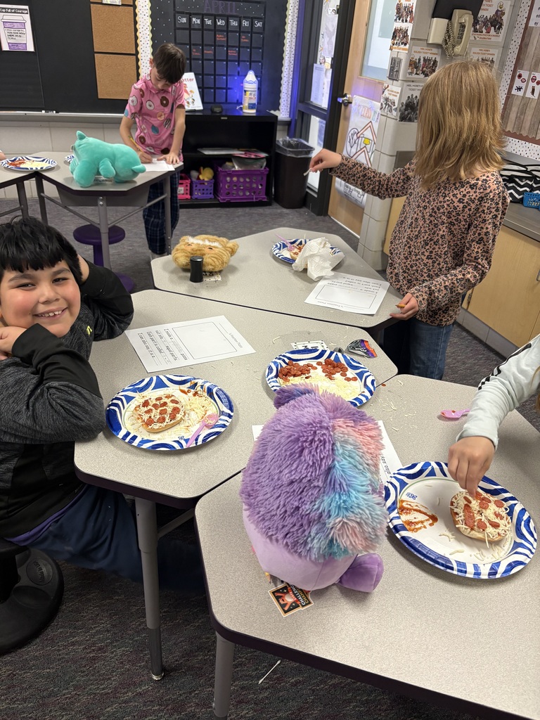A group of students working on making their pizzas on a bagel, almost done. One student noticed the camera and smiled.