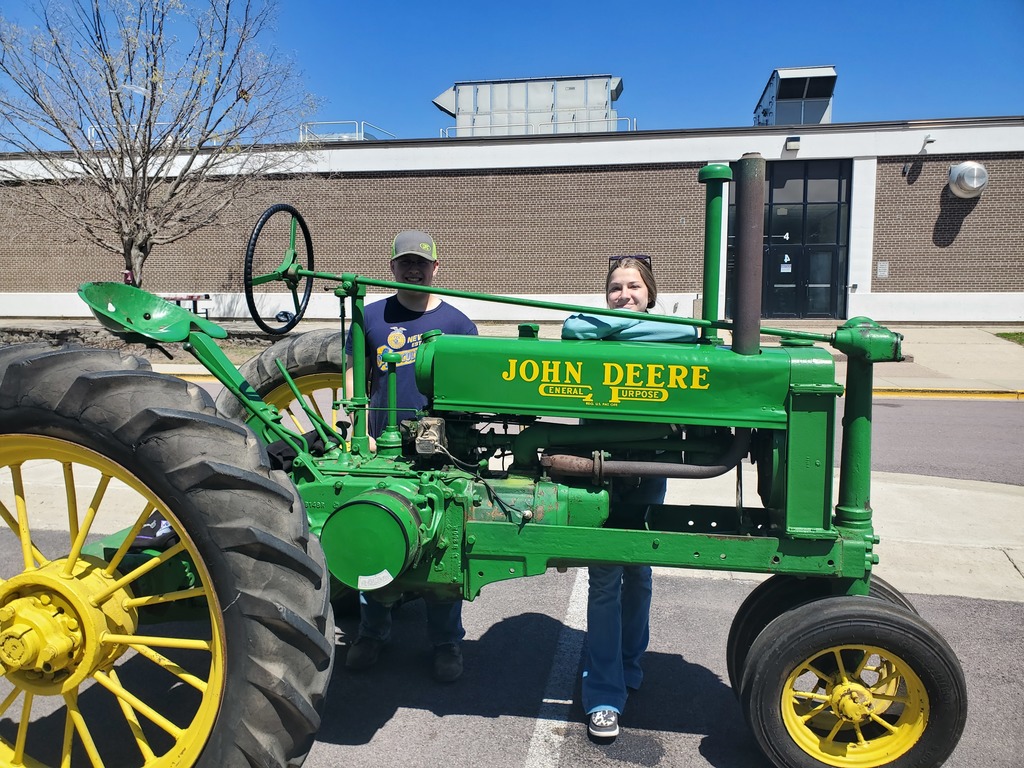 2 HS students behind a John Deere tractor.