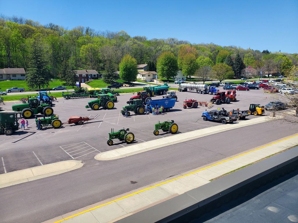 A rooftop view of several tractors and other farm vehicles in the Middle School parking lot, with a few students and staff about.