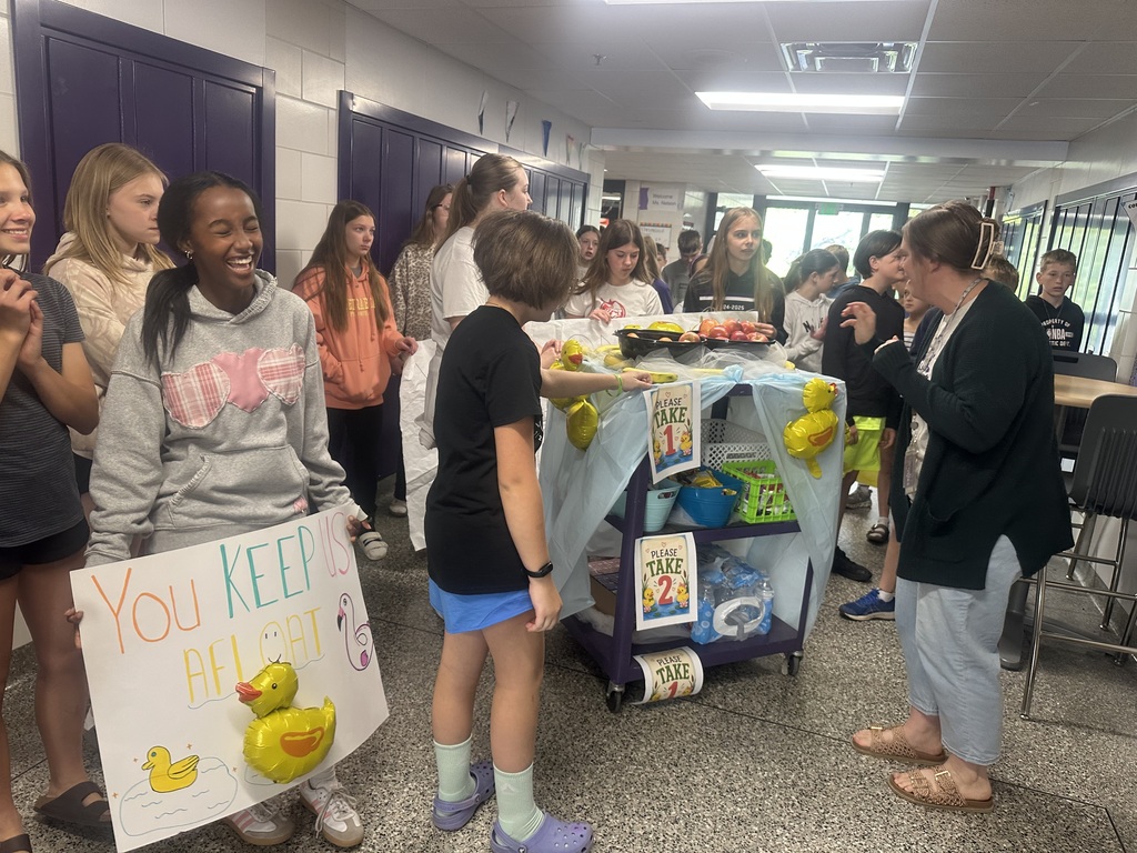 Students with their cart and teacher appreciation signs in a hallway, delivering fruit to more teachers