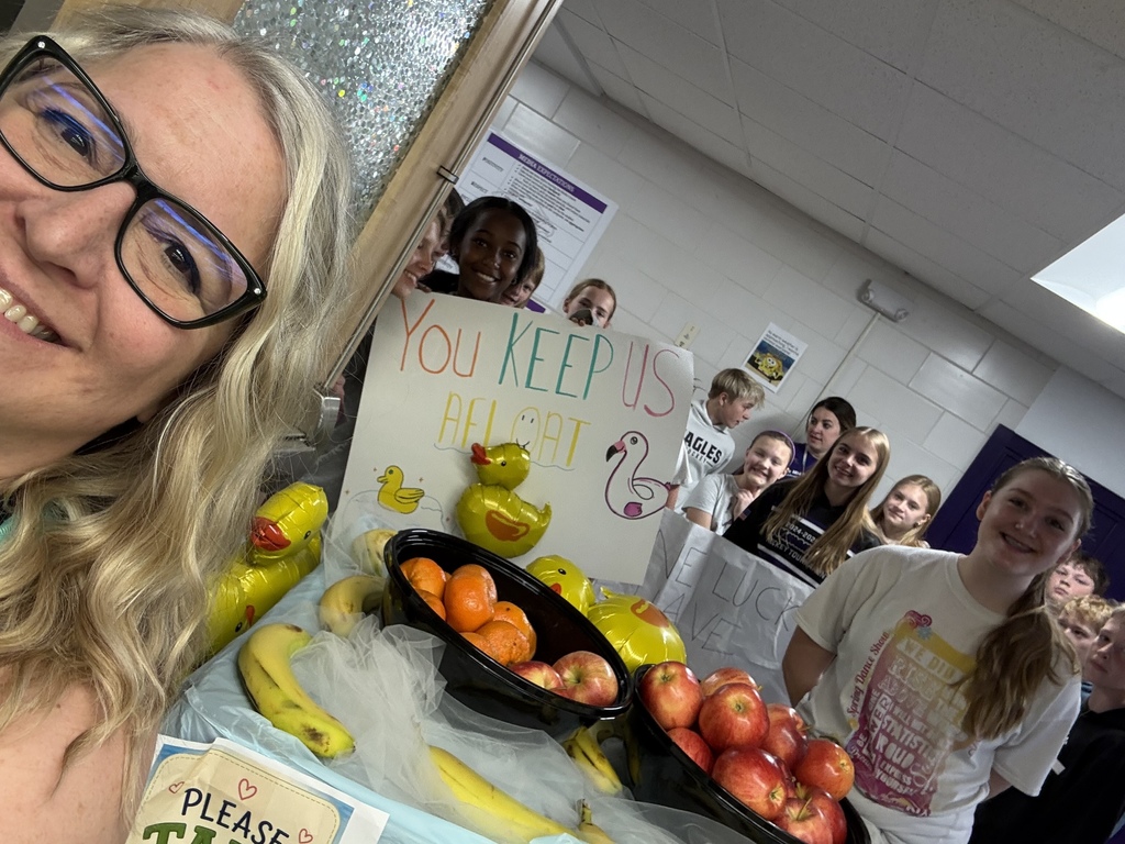 Mrs. Tam takes a selfie with students and their cart of fruit and balloon ducks, with the sign "You Keep Us Afloat"