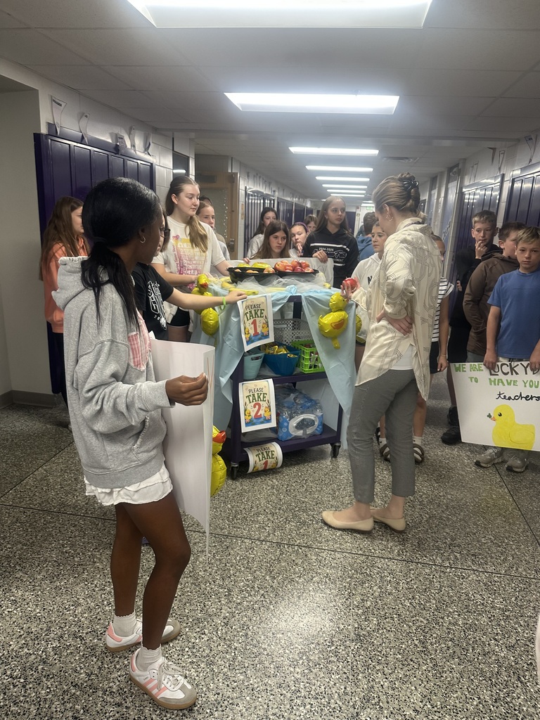 Students with their cart and teacher appreciation signs in a hallway, delivering fruit to more teachers.