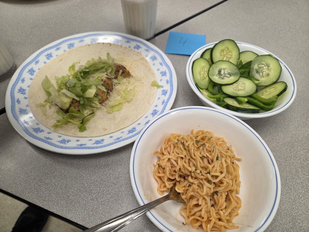 A plate with some kind of soft-shell taco, a bowl of cucumbers, and a bowl of pasta.