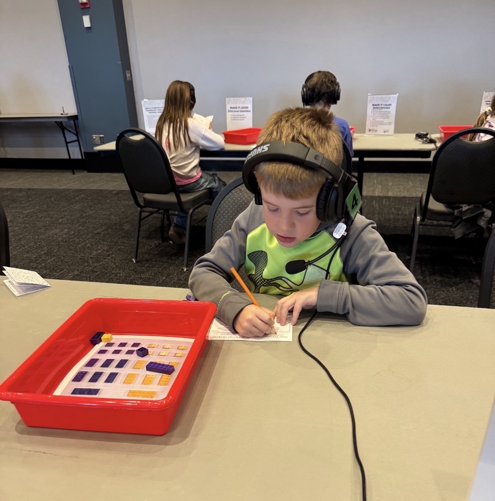 Students with headphones working on a worksheet at a hands-on exhibit.