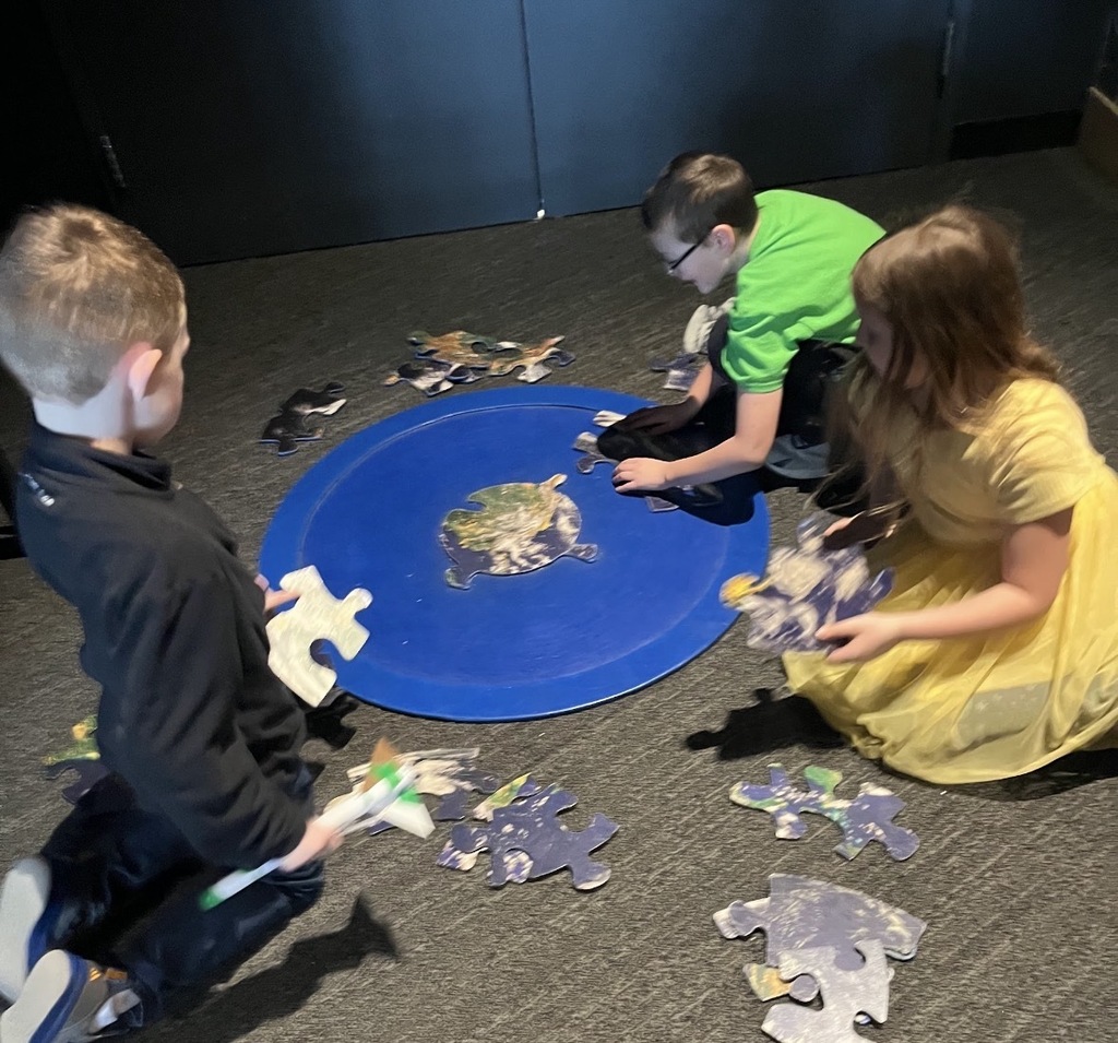 3 students working on a floor-puzzle with big pieces.
