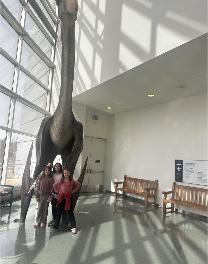 4 students pose for a picture in front of a model dinosaur.