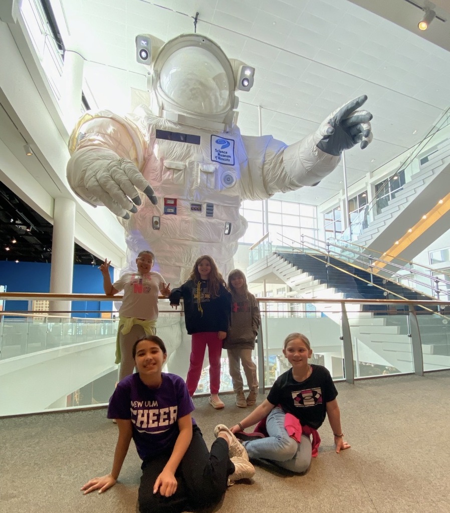 5 girls pose for a picture in front of the giant spacesuit in the center of the science museum.