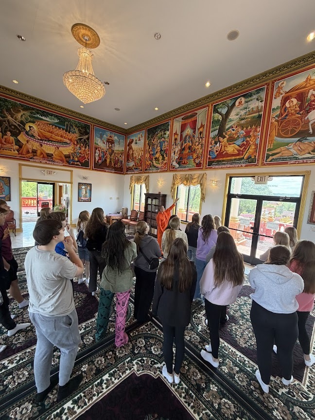 Group of students listening to their guide, pointing to paintings in the temple.