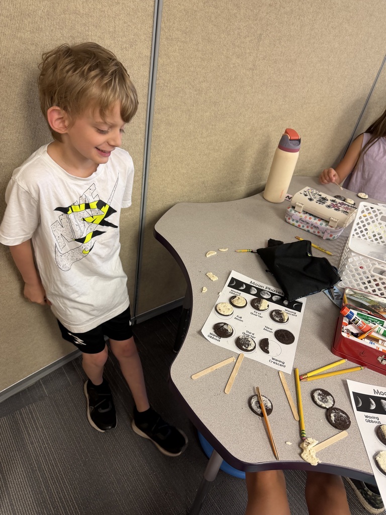 A student sheepishly looking at his moon phase cycle made out of oreos, a bite has been taken out of one of them.