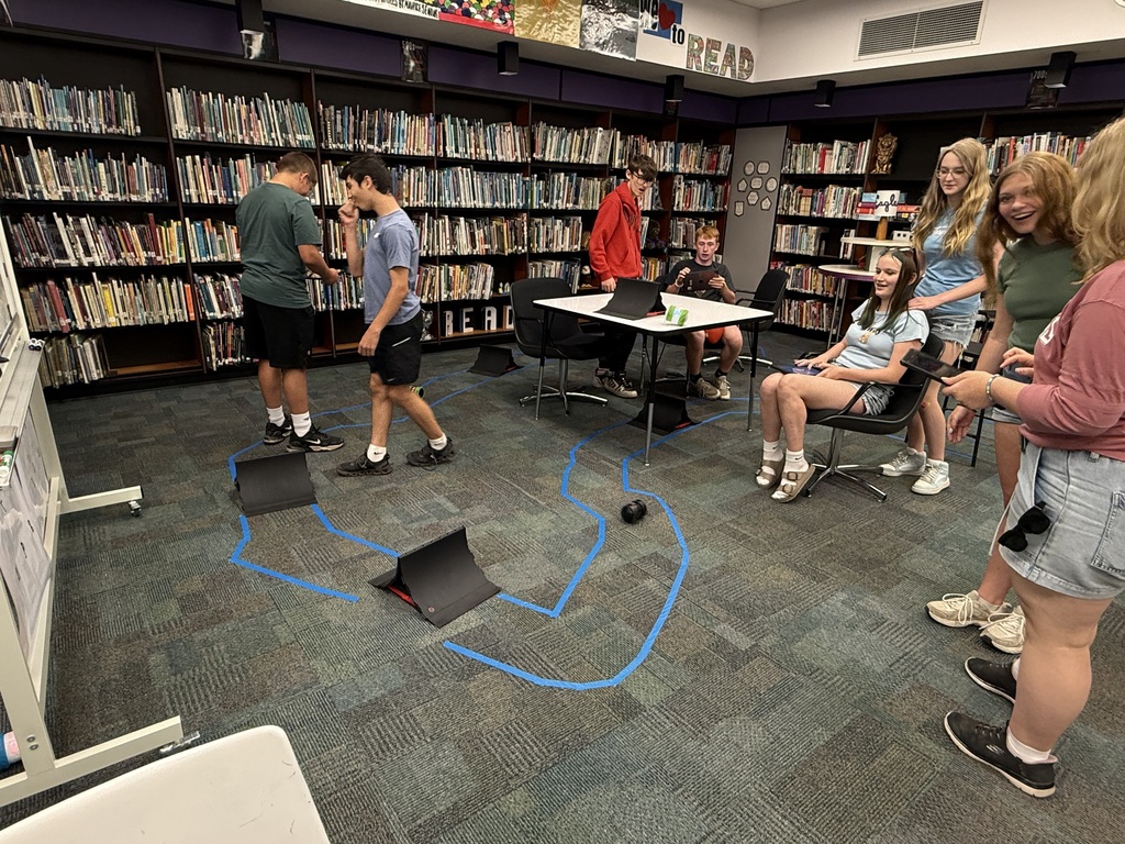 A bunch of students around a track with ramps and a robot.