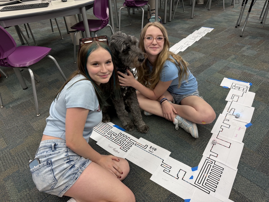 Two girls pose with Von the dog and the track they drew for their robot.