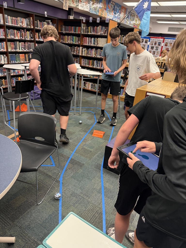 A few students controlling a couple different spherical robots using iPads, rolling them on the floor within the track and over ramps.