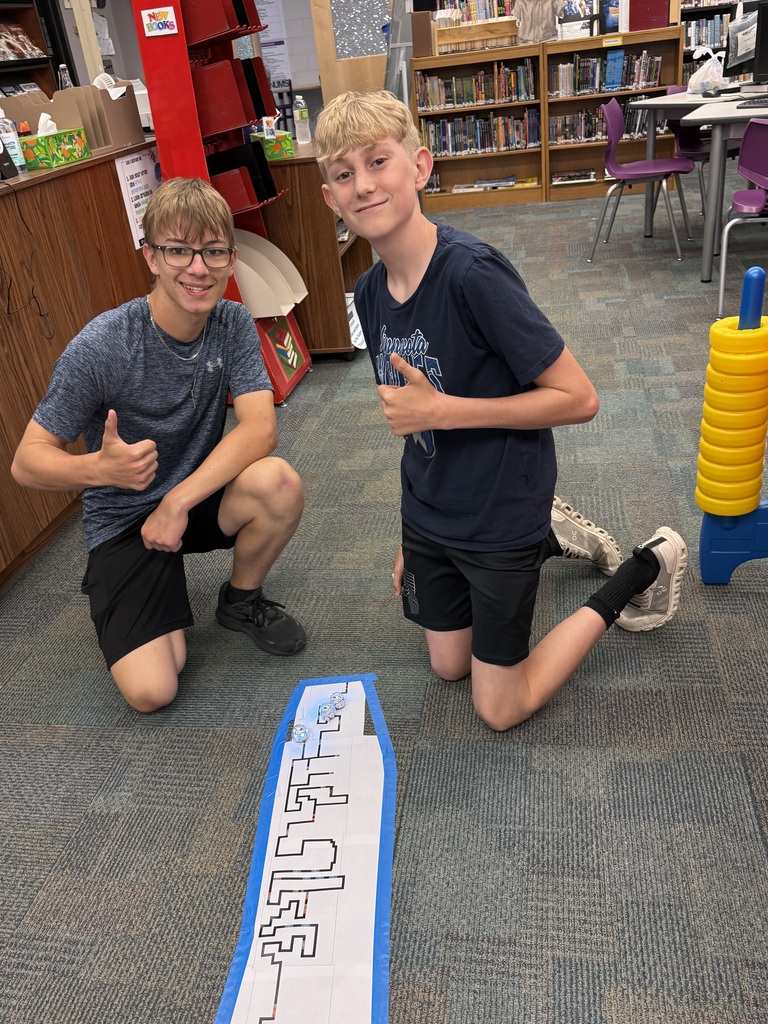 Two boys give thumbs up as their little robot travels down the track they drew.