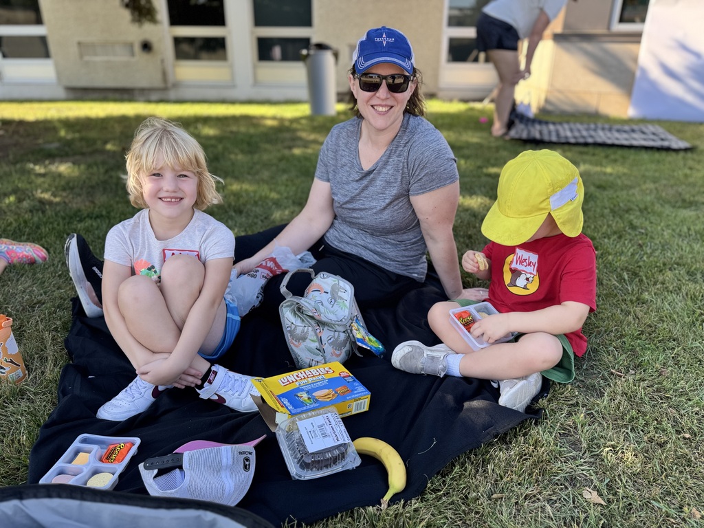 A woman and two children sit on a blanket having a picnic.