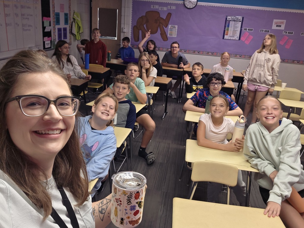 A selfie taken by the teacher with her students at their desks, smiling for the camera.
