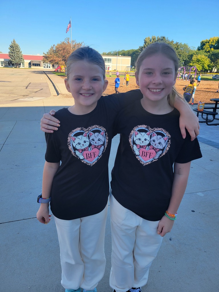 Two girls wearing matching black shirts with cat prints and white pants stand together on a sidewalk.