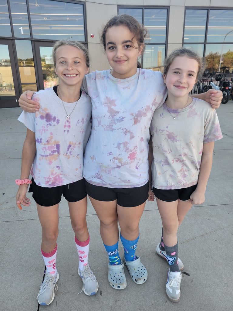 Three girls in tie-dye shirts and black shorts, smiling for a photo.