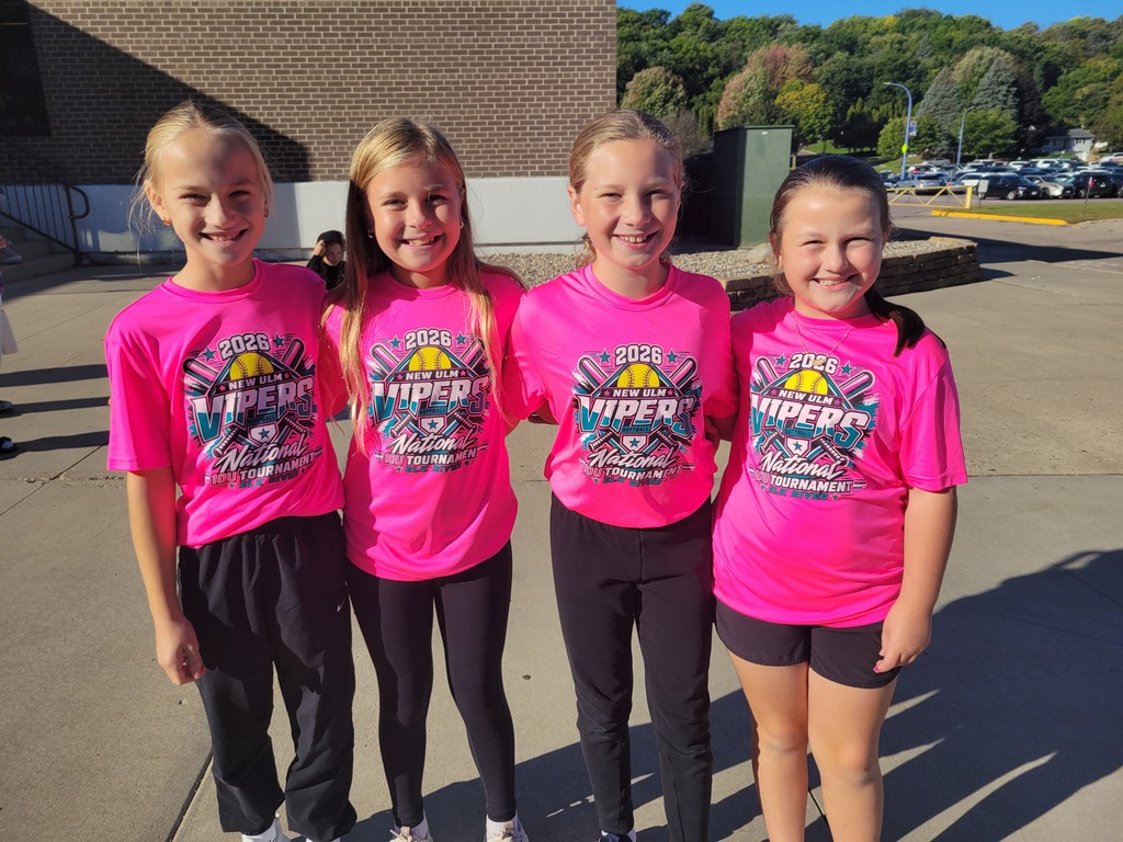 Four girls in matching pink shirts and black shorts/pants pose for a photo.