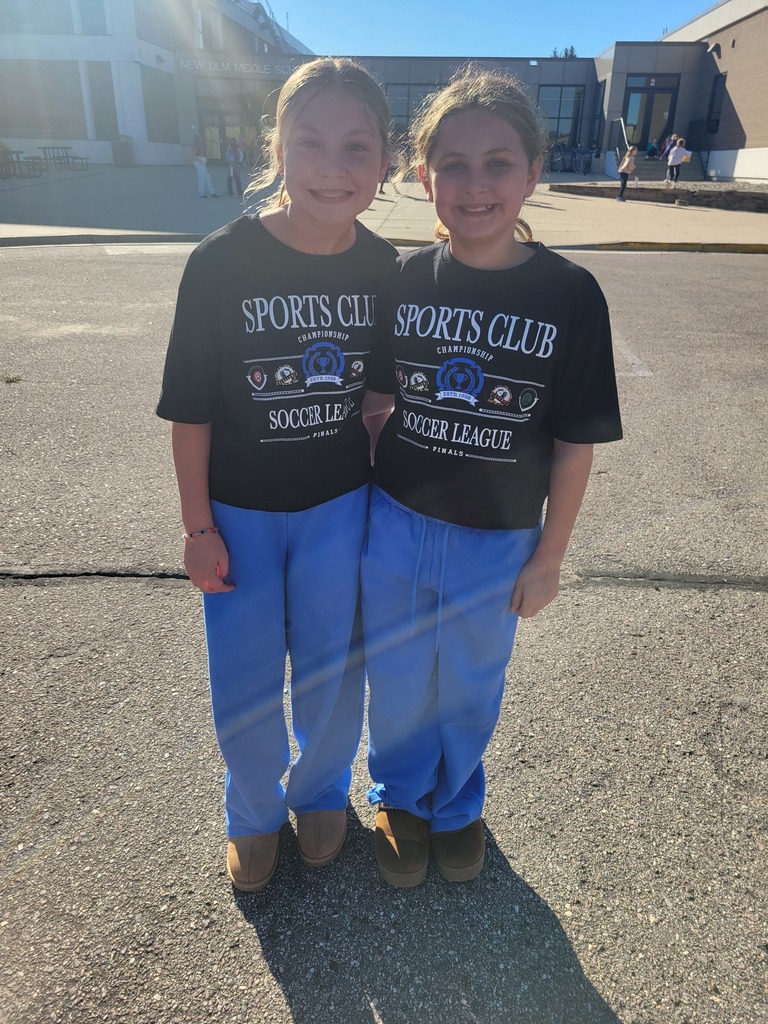 Two girls in matching shirts and pants pose in a parking lot. They stand close together, facing the camera.