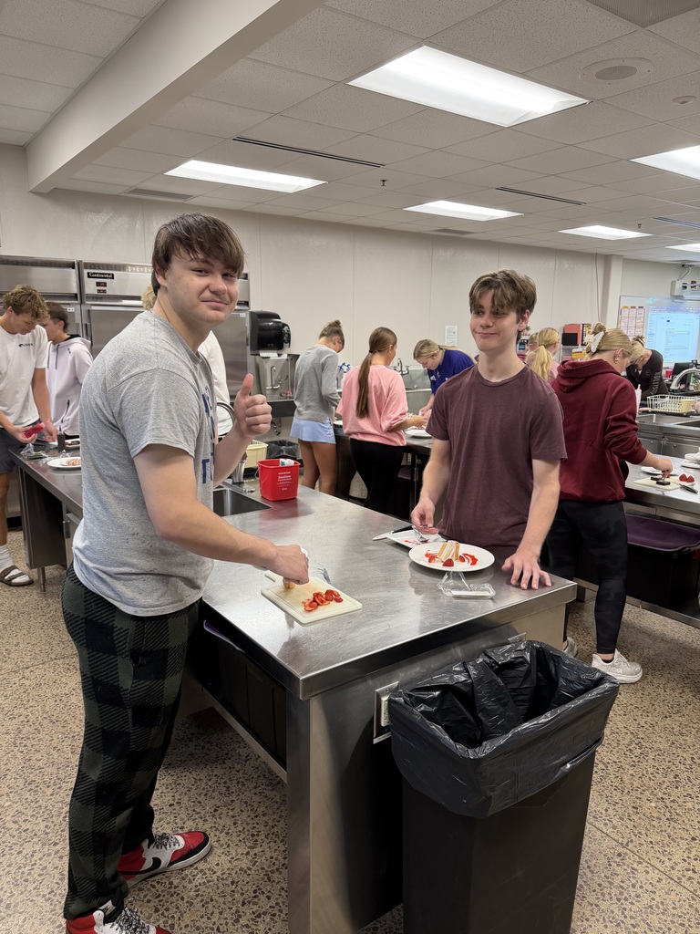 Two students in a kitchen with their plates, one student giving a thumbs up.